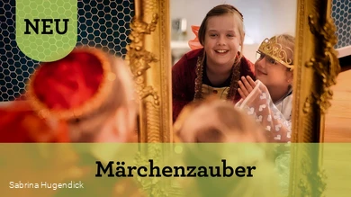 Zwei Mädchen in Prinzessinnenkleidern schauen lachend in einen golden umrandeten Spiegel